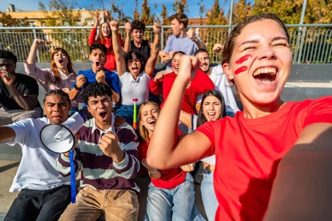Diverse group of young adult fans energetically cheering and celebrating a win at a sports event,
