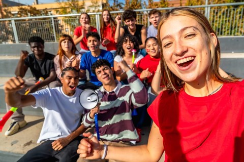 Cheering diverse group of young friends taking a stadium selfie while supporting their team,
