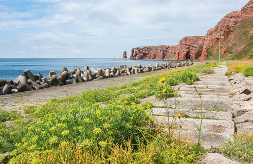 Wide, sunny coastline with concrete tetrapods by the sea, coastal protection, paved coastal strip