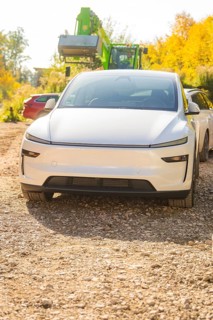 White electric car on a gravel path in autumn, surrounded by colorful foliage and trees, Telsa