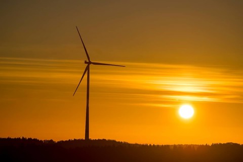 A single wind turbine in front of an intense orange sunset. The sky glows with bright colors,