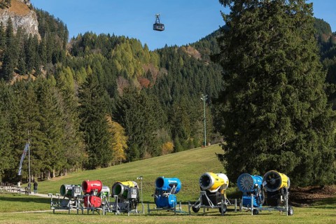 Snow cannons in a meadow surrounded by mountains and autumn forests, Tegelbergbahn cabin in the