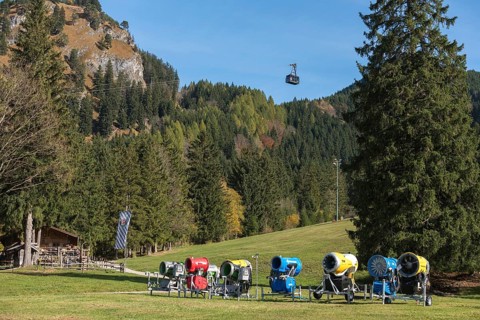 Snow cannons in front of a forest, mountains in the background, Tegelbergbahn cabin floating,