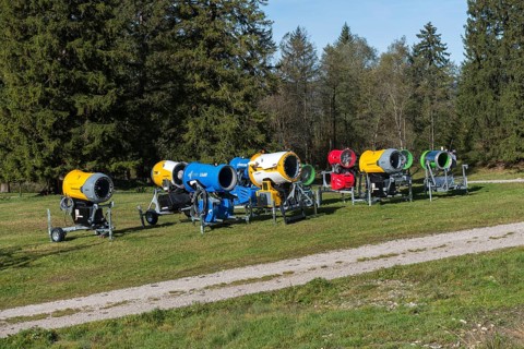 Row of snow cannons in a meadow in front of trees and blue sky, Schwangau near Füssen, Ostallgäu,