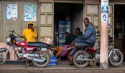 Street scene, people in front of a shop with their motorbikes waiting for the rain to end, Kisoro,