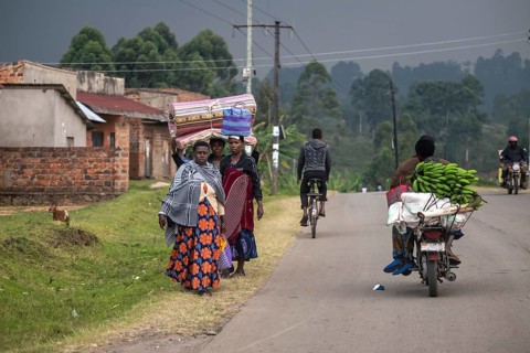 Street scene in rural Uganda, woman carrying bags and mattresses on their heads, motorcyclists