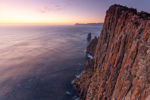 Long exposure at sunrise shows glowing dawn over the dramatic rocks on the Cape Hauy Track. Gentle