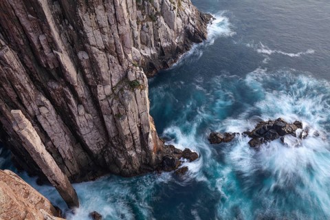 Long exposure at sunrise shows glowing dawn over the dramatic cliffs of Cape Hauy. Gentle waves hit