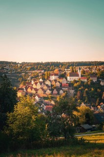 View of a village with church on a hill, warm sunlight shimmering through the trees, Altensteig,