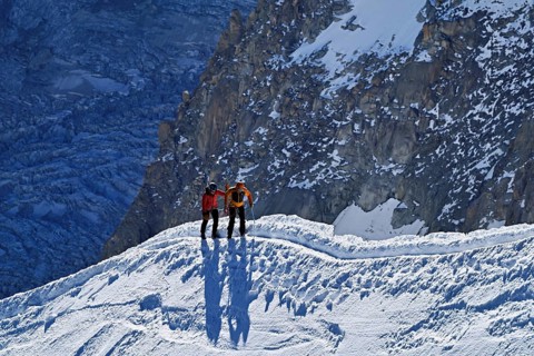 Two ascended mountaineers run across a snow-covered mountain ridge, Aiguille du Midi,