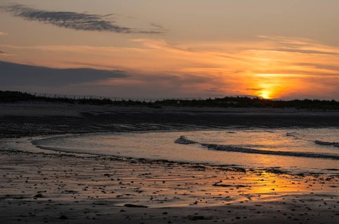 Sunset on a quiet beach with soft light on the waves, wet beach at low tide, dunes in the
