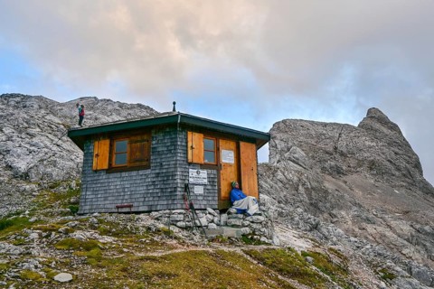 Two mountaineers relax at the Wildalmkirchl bivouac with the Wildalmkirchl summit in the
