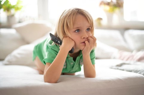 Child, boy, 7 years old, blonde, lying on sofa with remote control in hand, watching TV, watching
