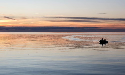 Angler on the beach during sunset, an angler docks on the shore with his inflatable boat and dog,