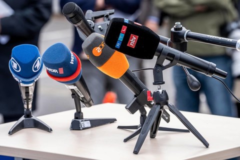 Microphones from various radio stations, television stations, standing on the table, at a press