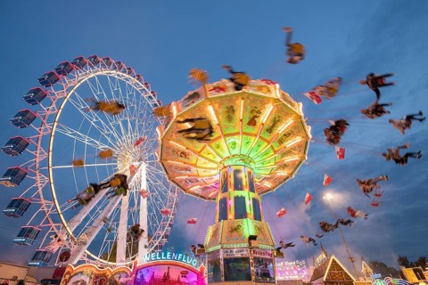 An illuminated chain carousel and Ferris wheel at night at a funfair, people swinging on chains,