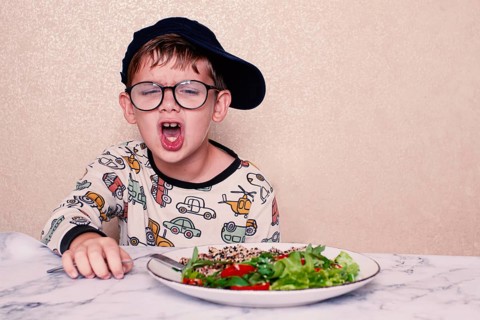 Child reacts dramatically to a salad served on a marble table at home during lunchtime, A little