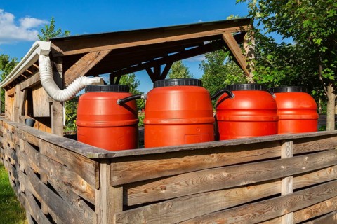 Reddish brown plastic water butts collecting and storing rain water from white plastic downspout in