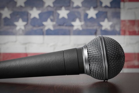 Microphone resting on a table with the american flag painted on A brick wall behind