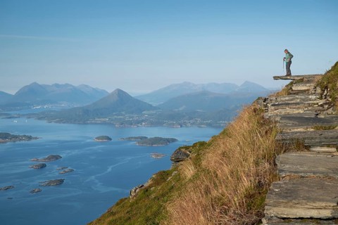 Woman with walking sticks standing on a ledge, Rørsethornet stone stairs, with 3292 steps one of