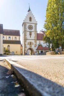 A historic tower with clock in a sunny street, surrounded by trees in autumn, Überlingen, Lake