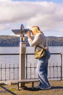 Woman looking through binoculars with a lake in the background, Überlingen, Lake Constance, Germany