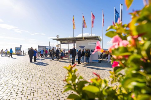 Crowd in front of a harbour building with flags and sunny cobblestones, Überlingen, Lake Constance,