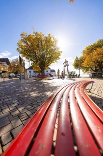 Red benches on a sunny town square surrounded by autumnal trees, Überlingen, Lake Constance,