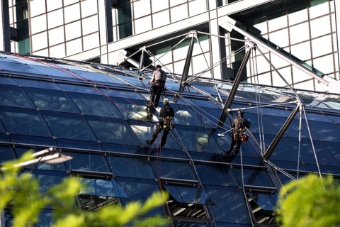 Three male glass cleaners abseiling down a glass roof of Berlin Central Station to clean windows,