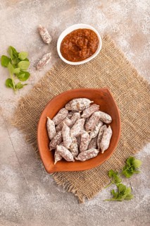 Small smoked Chicken sausages in clay bowl on brown concrete background and linen textile. top