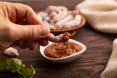 Small smoked Chicken sausages in wooden bowl with hand on brown wooden background and linen textile