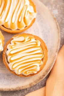 French lemon tart with meringue on brown concrete background, cup of coffee, orange linen textile,