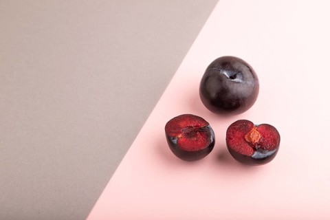 Purple Plum Cut in half on pink and gray pastel paper background. Side view, copy space. healthy