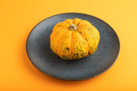 Orange Pumpkin on blue plate on orange pastel paper background. Side view, copy space, healthy