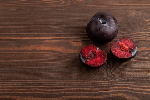 Purple Plum Cut in half on brown wooden background. Side view, copy space. healthy food, vegetable,