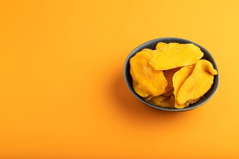 Dried Mango in blue ceramic bowl on orange pastel paper background. Side view, copy space. healthy