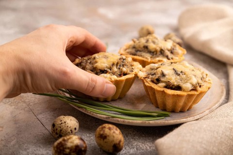 Tartlets with meat and cheese with hand on brown concrete background and linen textile. side view,