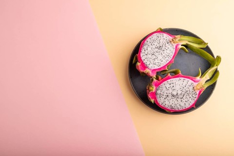 Ripe Pitaya on blue plate on pink and orange pastel paper background, top view, flat lay, copy