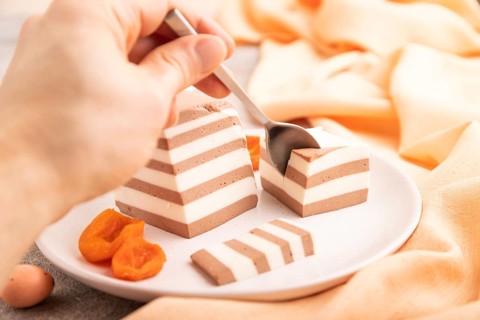 Cocoa and milk jelly with dried apricots with hand on brown concrete background and orange textile,