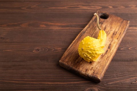 Decorative orange Pumpkin on cutting board on brown wooden background, side view, copy space,