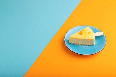 Yellow Cake pop with sprinkles on blue ceramic plate on blue and orange pastel paper background,