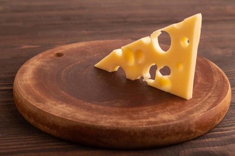 Piece of cheese with holes on cutting board on brown wooden background, side view, close up,