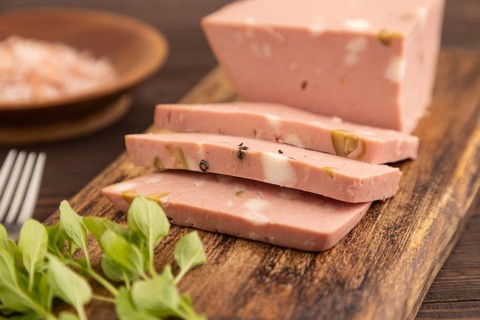 Mortadella sausage on wooden cutting board with pepper and herbs on brown wooden background. Side