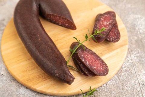 Sujuk sausage on wooden cutting board with pepper and herbs on brown concrete background. Side