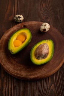 Two Avocado halves with pit and Egg yolk on round wooden cutting board on brown wooden, copy space,