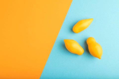 Yellow tomatoes on blue and orange pastel paper background. Top view, copy space, flat lay. healthy