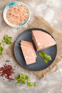 Mortadella sausage on plate with pepper and herbs on brown concrete background and linen textile.