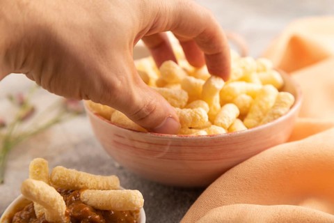 Corn flakes sticks with hand with caramel in ceramic bowl on gray concrete background and orange