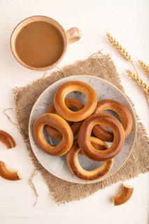 Homemade Ring Bagel with cup of coffee on white wooden background and linen textile. top view, flat