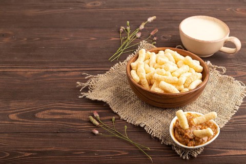 Corn flakes sticks with caramel in wooden bowl on brown wooden background and linen textile. Side